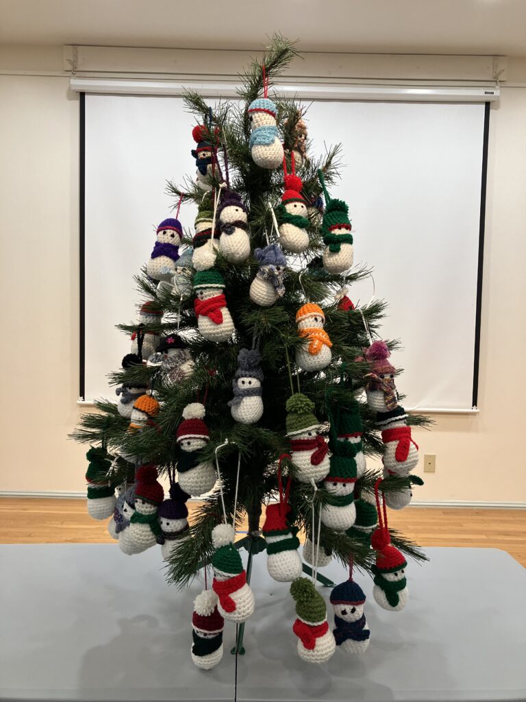 An image of the entire tree, about three feet tall, with about 30 different crochet snowmen covering the tree like ornaments in varying colors, from yellow to green to red and blue.